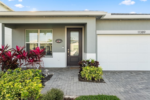 view of exterior entry featuring a garage, decorative driveway, and stucco siding