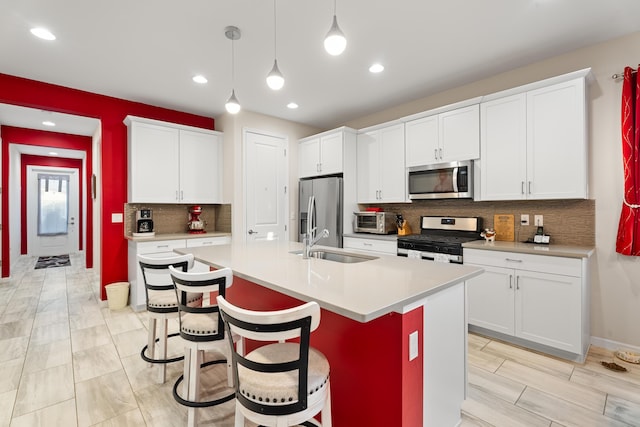 kitchen with an island with sink, hanging light fixtures, stainless steel appliances, light countertops, and a sink