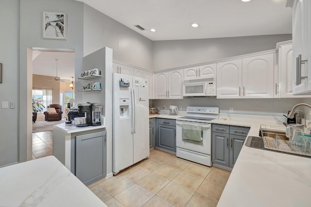 kitchen featuring light tile patterned flooring, gray cabinetry, white appliances, white cabinets, and light stone countertops