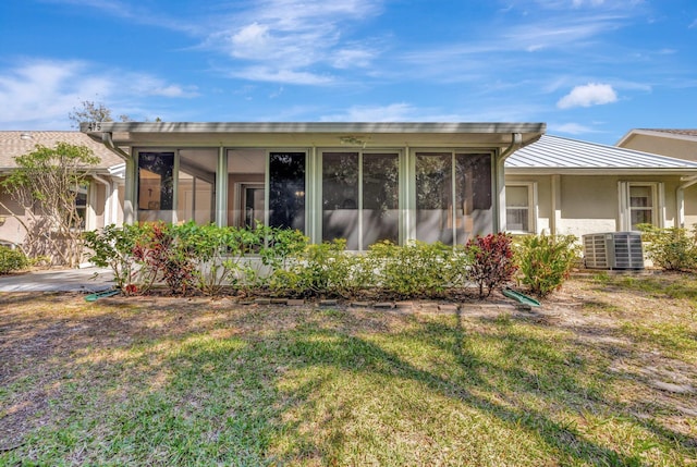 view of front facade featuring central AC unit, a front yard, a sunroom, a standing seam roof, and metal roof