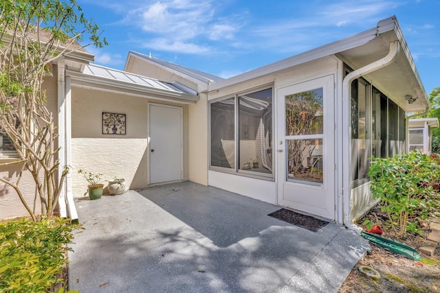 entrance to property featuring a standing seam roof, a patio area, metal roof, and stucco siding