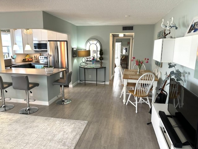 kitchen featuring dark wood-style floors, a breakfast bar area, visible vents, appliances with stainless steel finishes, and white cabinetry