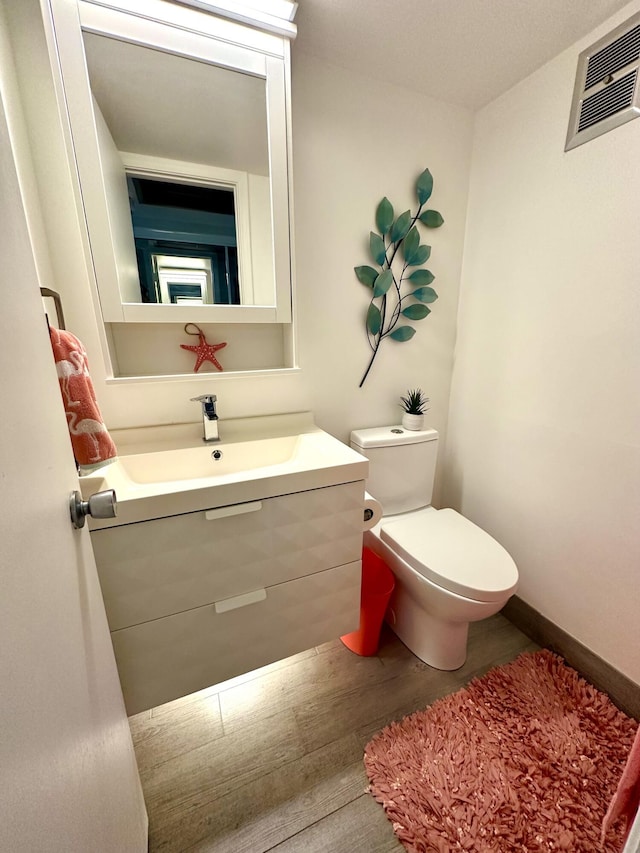 half bathroom with visible vents, toilet, vanity, wood finished floors, and baseboards