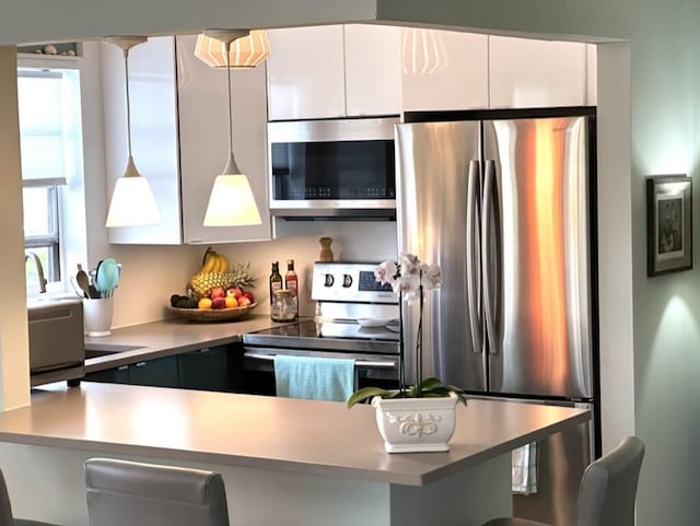 kitchen with a breakfast bar, white cabinets, light countertops, appliances with stainless steel finishes, and hanging light fixtures