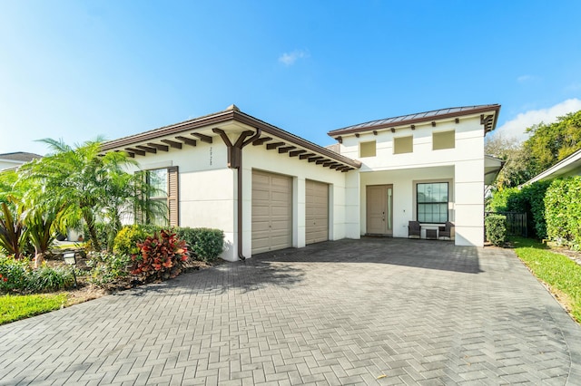 view of front of property featuring a garage, metal roof, a standing seam roof, decorative driveway, and stucco siding