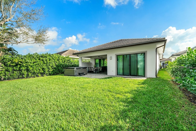 rear view of house featuring a yard, a patio, stucco siding, and a hot tub