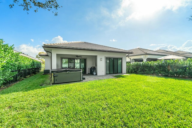 back of house featuring a yard, stucco siding, a hot tub, ceiling fan, and a fenced backyard