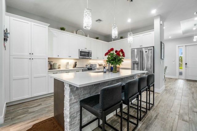 kitchen featuring stainless steel appliances, a kitchen island with sink, light countertops, and white cabinetry