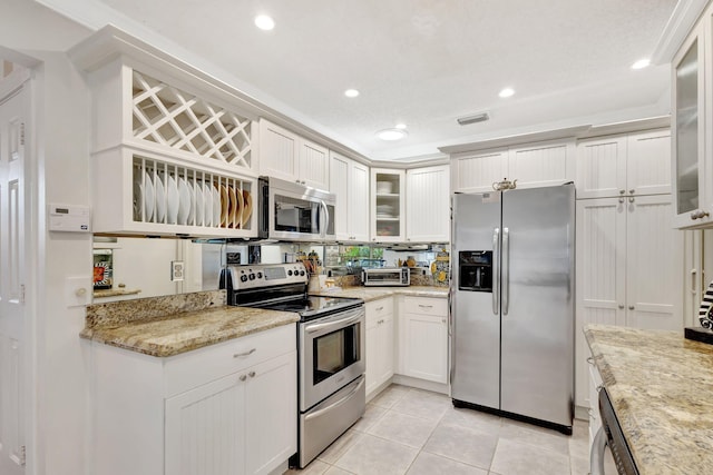 kitchen with light stone counters, visible vents, white cabinets, appliances with stainless steel finishes, and glass insert cabinets