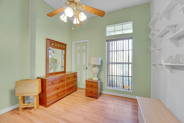 bedroom featuring baseboards, ceiling fan, a high ceiling, and light wood-style floors