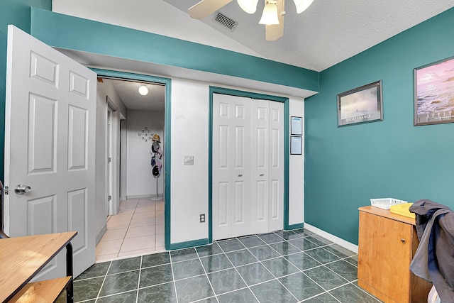 interior space featuring a textured ceiling, dark tile patterned flooring, visible vents, baseboards, and a closet