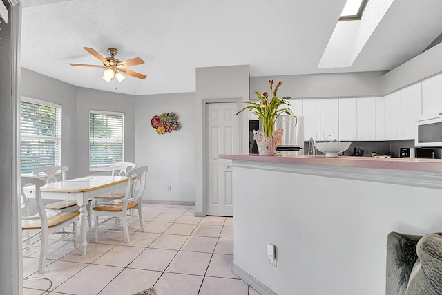 kitchen with a skylight, white microwave, freestanding refrigerator, white cabinetry, and light tile patterned flooring