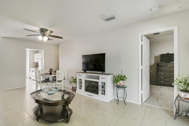 living area with light tile patterned floors, a fireplace, visible vents, and a ceiling fan