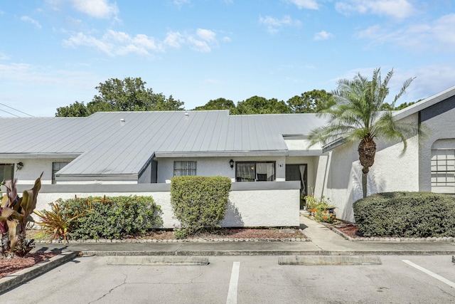 view of front of home featuring metal roof, a fenced front yard, stucco siding, uncovered parking, and a standing seam roof