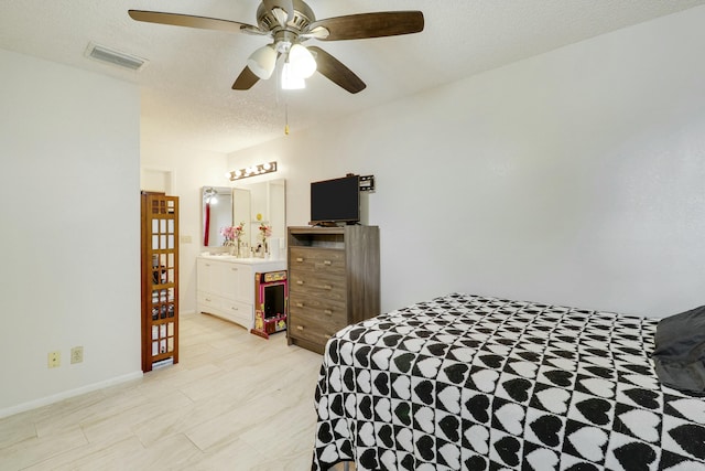 bedroom with light wood finished floors, visible vents, ensuite bathroom, ceiling fan, and a textured ceiling