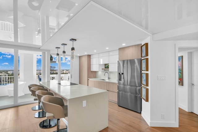 kitchen with a kitchen island, white cabinetry, light countertops, stainless steel refrigerator with ice dispenser, and modern cabinets