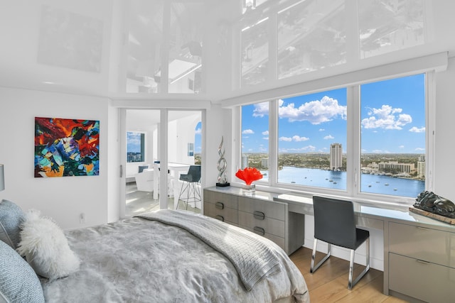 bedroom featuring a water view, light wood-style floors, and built in study area