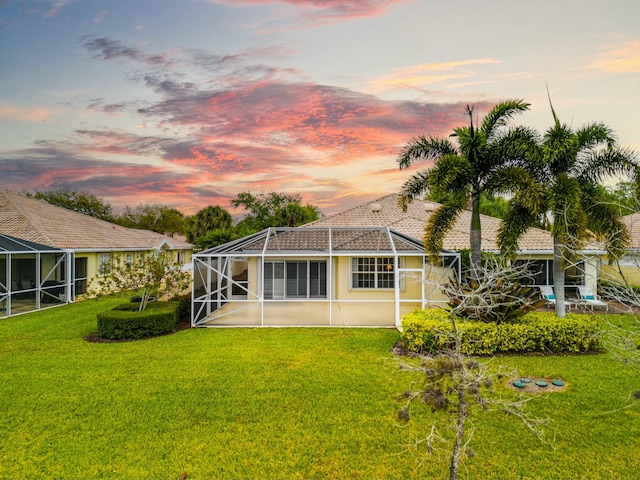 back of property at dusk featuring glass enclosure, a yard, and stucco siding