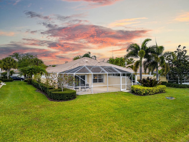 back of house at dusk featuring a lanai and a yard