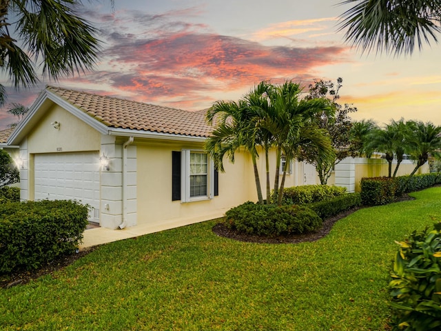 property exterior at dusk featuring a tiled roof, a lawn, an attached garage, and stucco siding