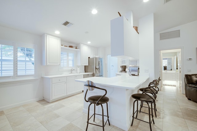 kitchen with stainless steel fridge with ice dispenser, a kitchen breakfast bar, a peninsula, light countertops, and white cabinetry