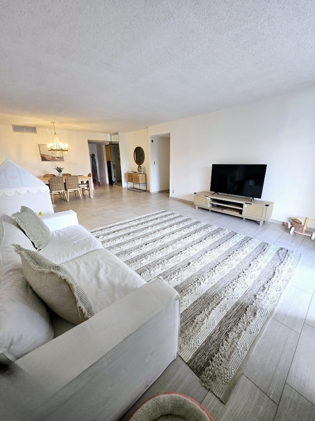 living room featuring a chandelier, a textured ceiling, wood finished floors, visible vents, and baseboards