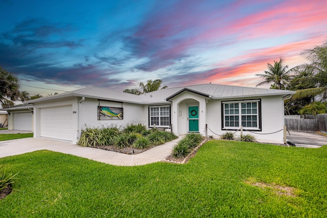 single story home with concrete driveway, a lawn, metal roof, an attached garage, and stucco siding