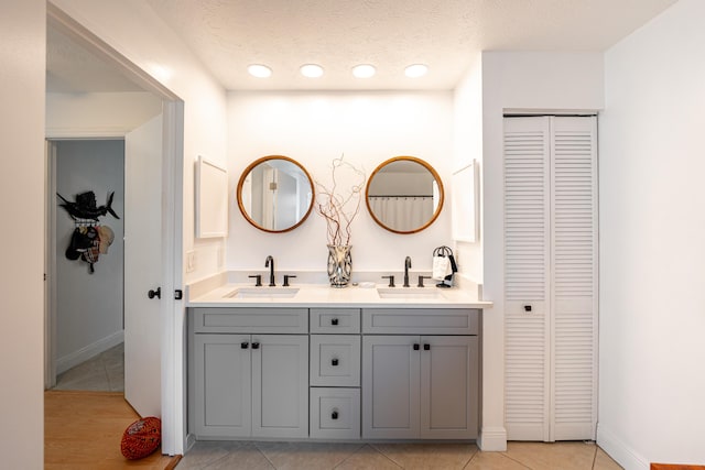 bathroom with a sink, a textured ceiling, double vanity, and a closet