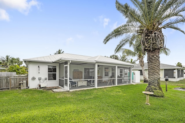 back of property featuring stucco siding, a lawn, a sunroom, metal roof, and fence