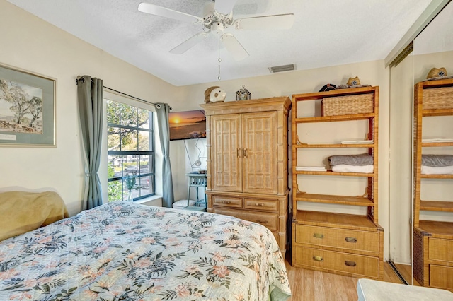 bedroom featuring light wood-style floors, ceiling fan, visible vents, and a textured ceiling