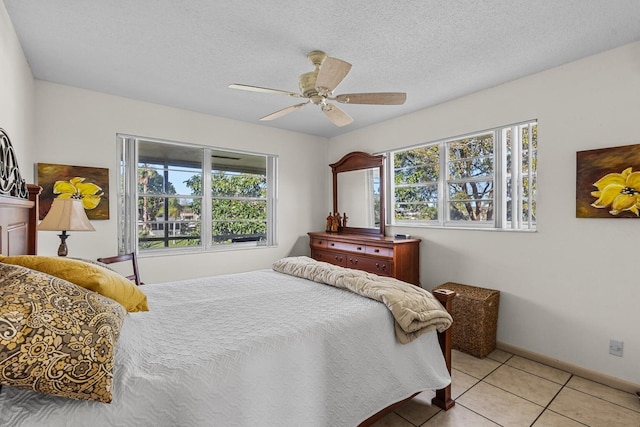 bedroom featuring a ceiling fan, a textured ceiling, baseboards, and light tile patterned floors