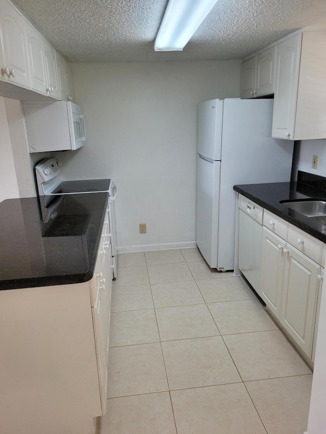 kitchen with a textured ceiling, white appliances, light tile patterned flooring, white cabinets, and baseboards
