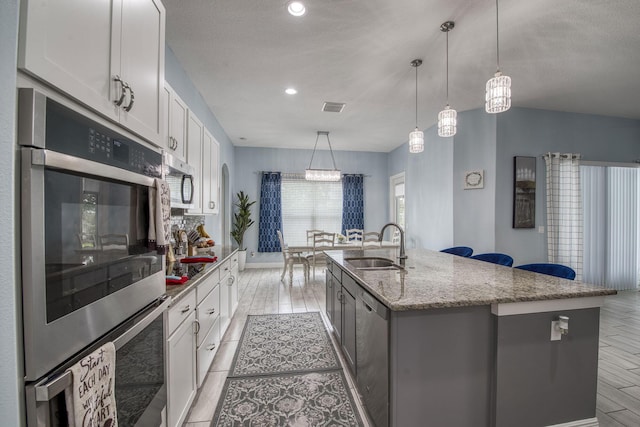 kitchen featuring decorative light fixtures, stainless steel appliances, white cabinets, a kitchen island with sink, and a sink