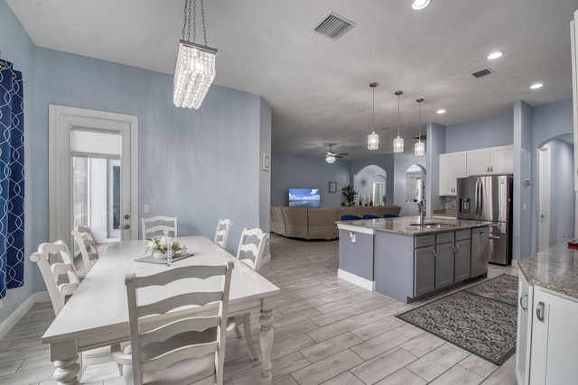 kitchen with arched walkways, decorative light fixtures, a center island with sink, gray cabinets, and stainless steel fridge with ice dispenser