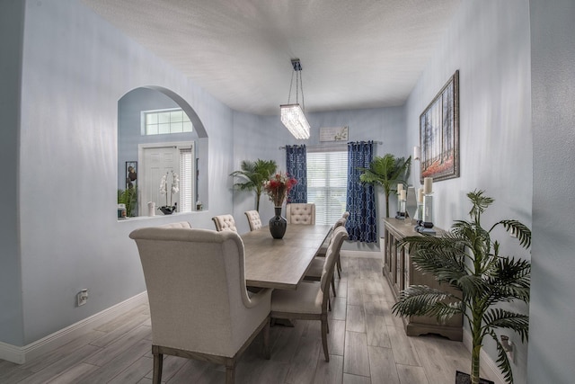 dining space featuring arched walkways, wood finish floors, a textured ceiling, and baseboards