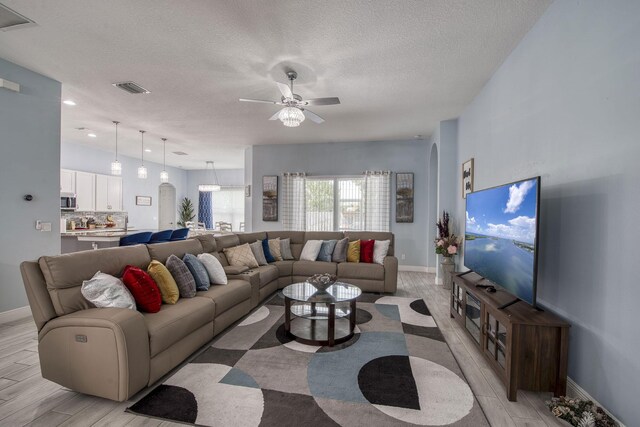 living area with a textured ceiling, ceiling fan, arched walkways, visible vents, and light wood finished floors