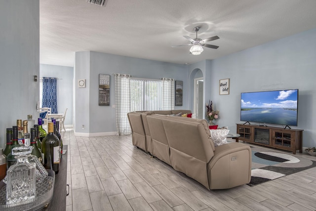 living area featuring arched walkways, ceiling fan, a textured ceiling, wood finish floors, and baseboards