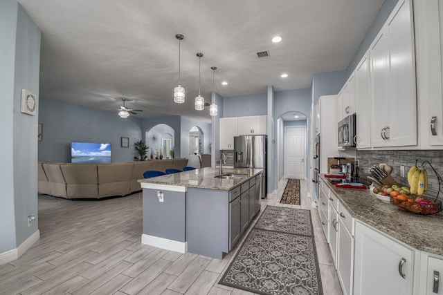 kitchen featuring arched walkways, appliances with stainless steel finishes, open floor plan, white cabinetry, and a sink