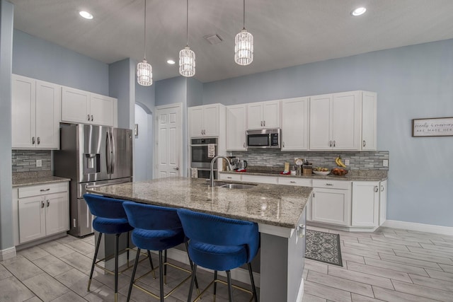 kitchen featuring arched walkways, appliances with stainless steel finishes, a sink, and white cabinetry