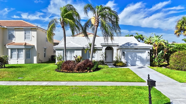 mediterranean / spanish home featuring a front lawn, a tile roof, concrete driveway, stucco siding, and an attached garage