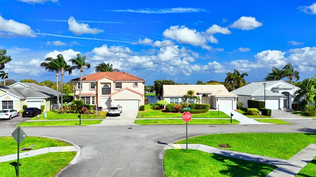 ranch-style home with driveway, a tile roof, an attached garage, a front yard, and stucco siding