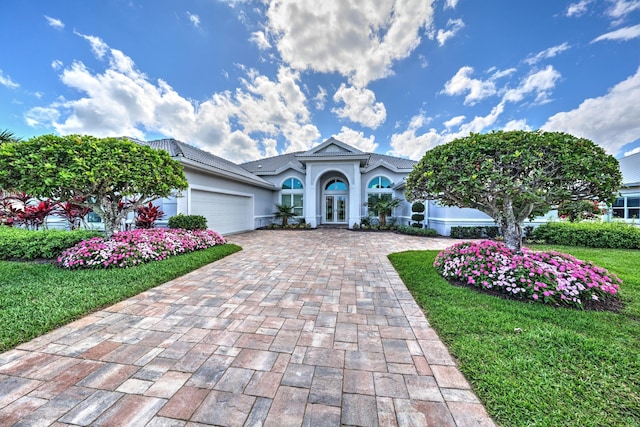 view of front facade with a tiled roof, an attached garage, decorative driveway, french doors, and stucco siding