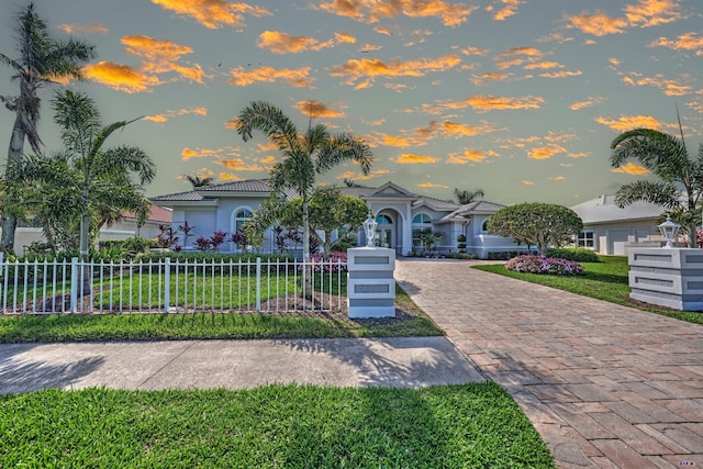 view of front facade with a fenced front yard, a tile roof, decorative driveway, a yard, and stucco siding