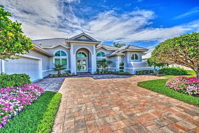 mediterranean / spanish-style home with driveway, stucco siding, an attached garage, and french doors