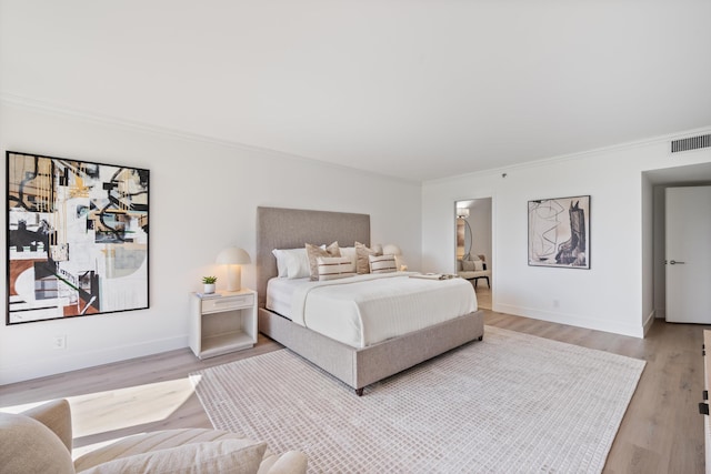 bedroom with baseboards, wood finished floors, visible vents, and crown molding