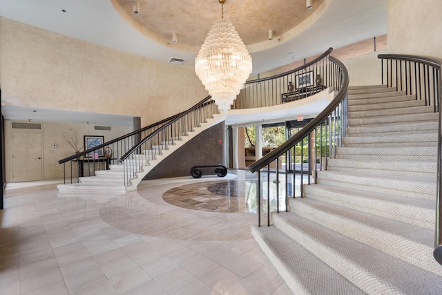 stairway featuring visible vents, a high ceiling, a chandelier, and a raised ceiling