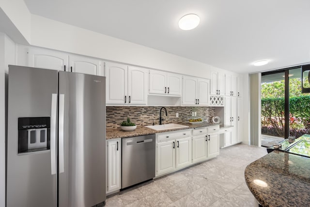 kitchen with stone countertops, white cabinets, appliances with stainless steel finishes, a sink, and backsplash