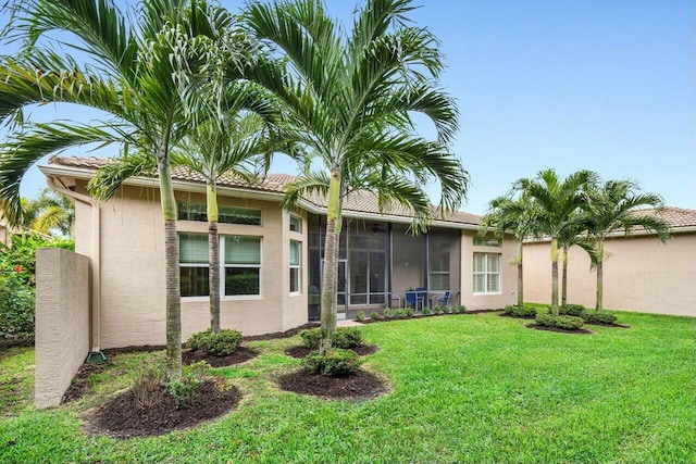 view of front of house featuring a front lawn, a tile roof, a sunroom, and stucco siding