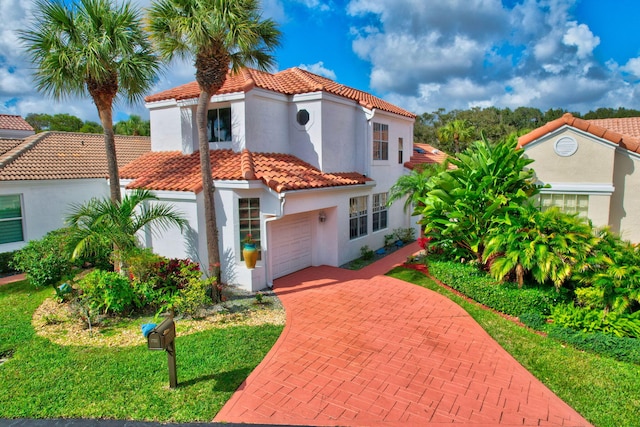 mediterranean / spanish home with decorative driveway, a tile roof, stucco siding, a front yard, and a garage