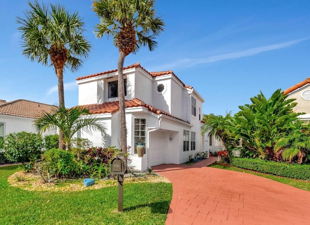 mediterranean / spanish home featuring a garage, a tile roof, decorative driveway, stucco siding, and a front lawn